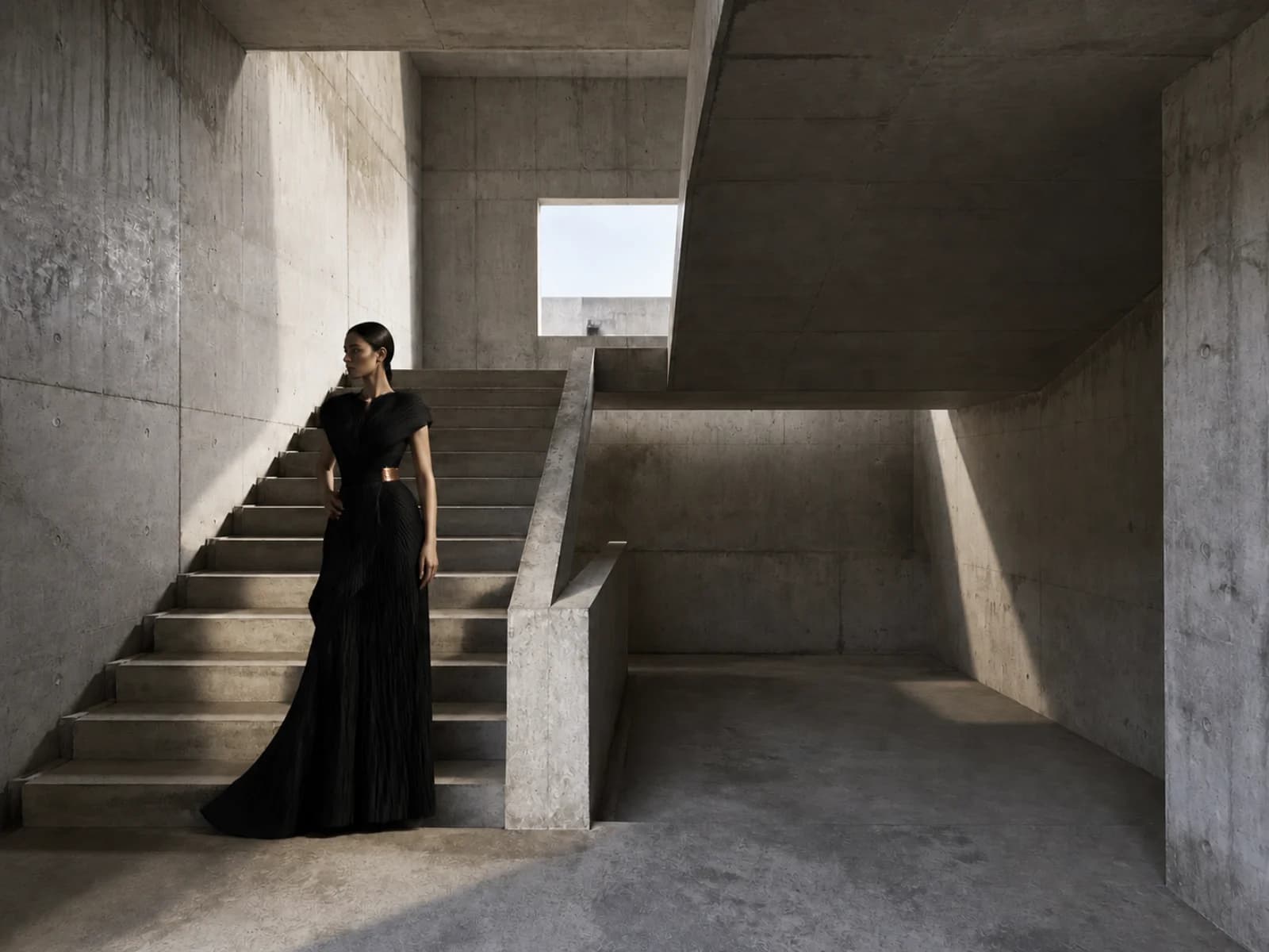 Model in a sculptural black dress inside a brutalist concrete stairwell